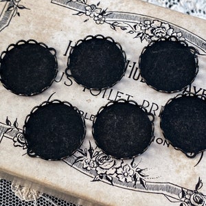 May include: Six black metal round tray or bezel settings with scalloped edges. The trays are on a vintage box with floral designs.