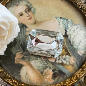 Puede incluir: Un cristal de vidrio transparente de forma rectangular con bordes biselados, descansando sobre un marco de imagen vintage con un retrato de una mujer con un vestido blanco.