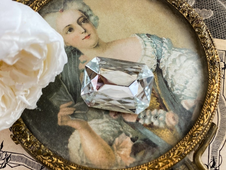 Puede incluir: Un cristal de vidrio transparente de forma rectangular con bordes biselados, descansando sobre un marco de imagen vintage con un retrato de una mujer con un vestido blanco.
