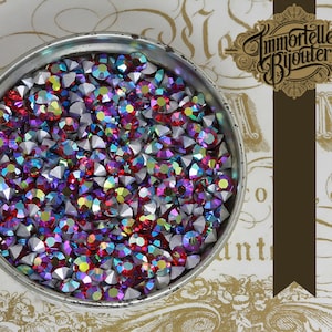 May include: A close-up of a silver container filled with iridescent red, blue, and silver rhinestones. The rhinestones are small and have a faceted design.