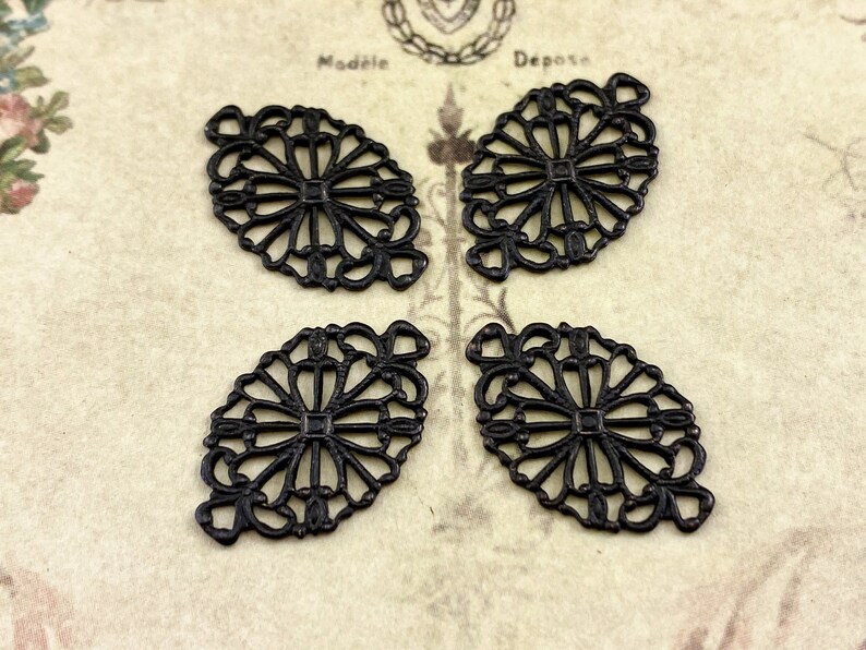 Puede incluir: Cuatro adornos de metal negro filigranados con un dise&ntilde;o floral. Cada adorno tiene forma ovalada con un centro decorativo.