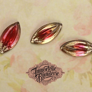 May include: Three red glass teardrop-shaped buttons with gold-colored metal trim. The buttons have a raised design and a slightly iridescent finish.