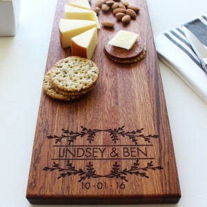 May include: Personalized wooden serving board with the names Lindsey & Ben and the date 10-01-16 engraved on it. The board is decorated with a floral design and features cheese, crackers, and almonds.