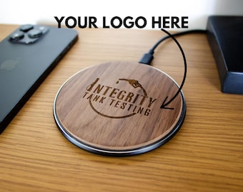 May include: A round wireless charger with a wooden surface and a silver trim. The charger has the text "INTEGRITY TANK TESTING" and a logo etched into the wood. A black phone and a black device are in the background. The text "YOUR LOGO HERE" is at the top.