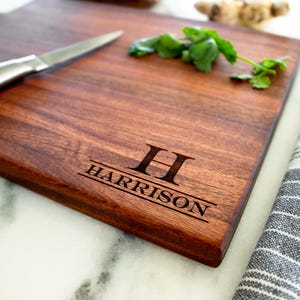 May include: A personalized wooden cutting board with the name "HARRISON" and the initial "H" engraved on it. The board is brown and has a natural wood grain.