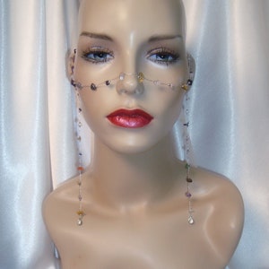 May include: A mannequin wearing a silver chain nose piece with colorful gemstones. The chain is attached to two long strands of beads that hang down the sides of the neck.