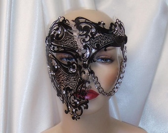 May include: A black masquerade mask with rhinestones and a chain. The mask is on a white mannequin head.