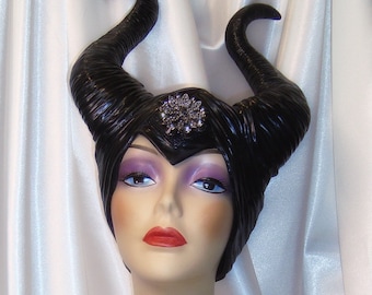 May include: A black, sculpted headdress with horns, resembling the character Maleficent from the Disney movie Sleeping Beauty. The headdress is worn by a mannequin with a white background.