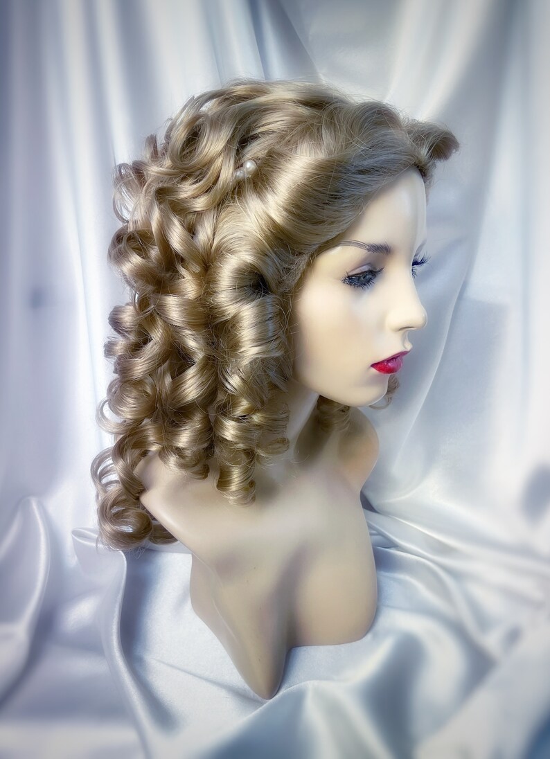 May include: A blonde wig with large curls styled in a vintage updo. The wig is on a mannequin head and has a few small white pearl accents.