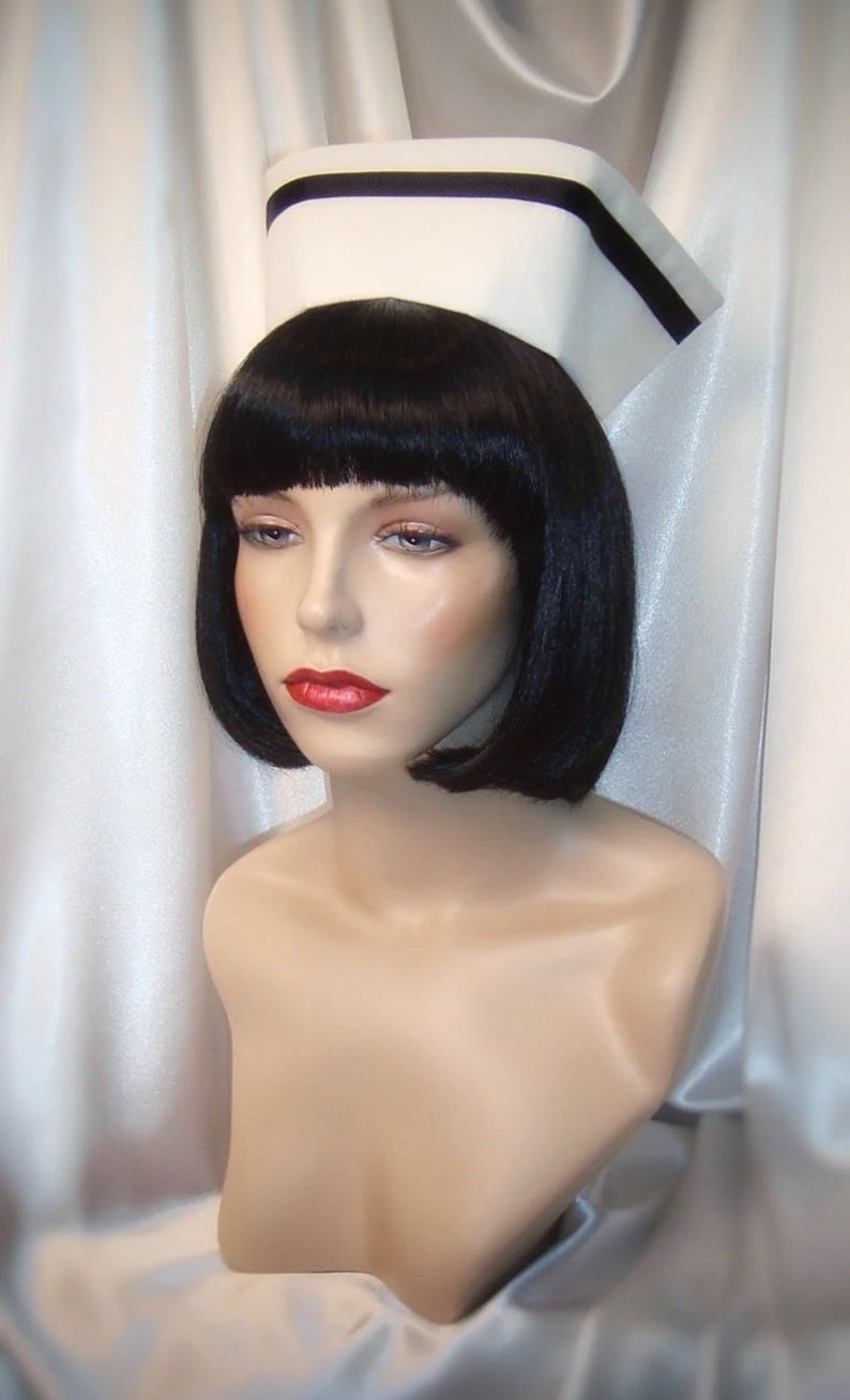 May include: A white nurse's cap with a black band, worn by a mannequin with black hair and red lipstick.