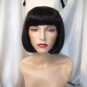 May include: A white nurse's cap with a black band, worn by a mannequin with black bobbed hair and red lipstick.