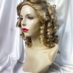 May include: A blonde wig with large curls styled in a vintage updo. The wig is on a mannequin head and has a natural-looking finish.