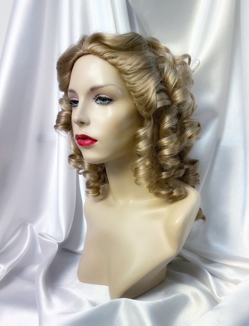 May include: A blonde wig with large curls styled in a vintage updo. The wig is on a mannequin head and has a natural-looking finish.