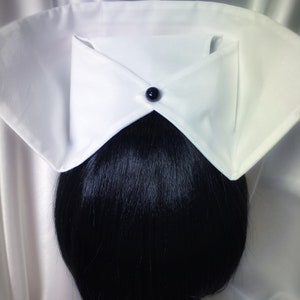 May include: White nurse's cap with a black button on the front. The cap is folded in a triangular shape and is worn over a black ponytail.