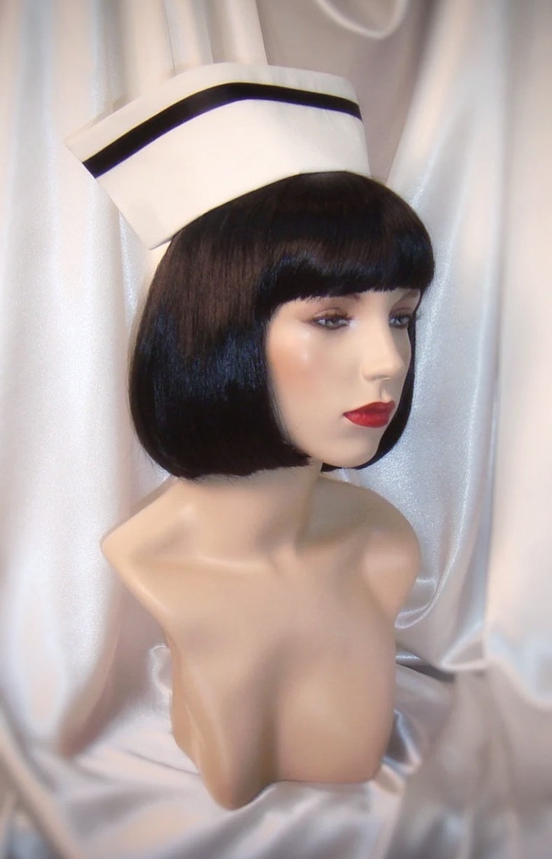 May include: A white nurse's cap with a black band around the crown. The cap is on a mannequin with black bobbed hair and red lipstick.
