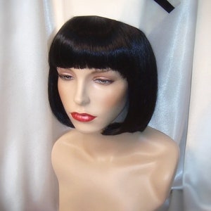 May include: A white nurse's cap with a black band around the brim. The cap is on a mannequin with black hair styled in a bob.