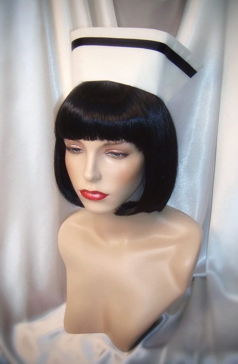 May include: A white nurse's cap with a black band around the brim. The cap is on a mannequin with black hair styled in a bob.