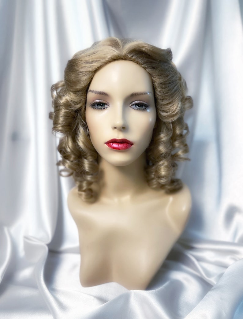 May include: A blonde wig with loose curls styled in a vintage updo. The wig is on a mannequin head and has a natural-looking finish.