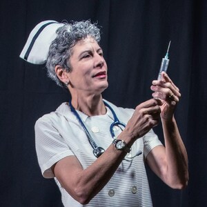 May include: A woman wearing a white nurse's uniform and a white cap with a blue stripe holds a syringe with a needle. She is wearing a watch on her left wrist and a stethoscope around her neck.
