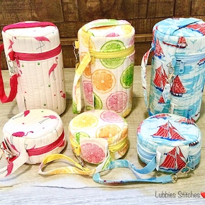 May include: A collection of quilted fabric bottle holders and matching round pouches. The holders feature flamingo, citrus fruit, and sailboat patterns. Each has a zipper closure and a wrist strap. The text "Lubbies Stitches" is visible.