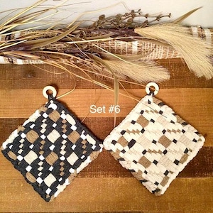 May include: Two woven pot holders with wooden ring hangers. One is black, tan, and white, the other is cream, tan, and white. The text "Set #6" is visible. The pot holders are square with a woven pattern.