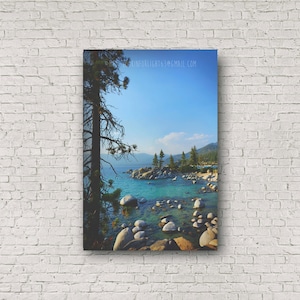 May include: A scenic view of a lake with turquoise water, surrounded by rocks and trees. The water is clear and calm, and the sky is a bright blue. The image is taken from a high vantage point, looking down at the lake.