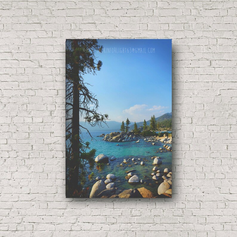 May include: A scenic view of a lake with turquoise water, surrounded by rocks and trees. The water is clear and calm, and the sky is a bright blue. The image is taken from a high vantage point, looking down at the lake.