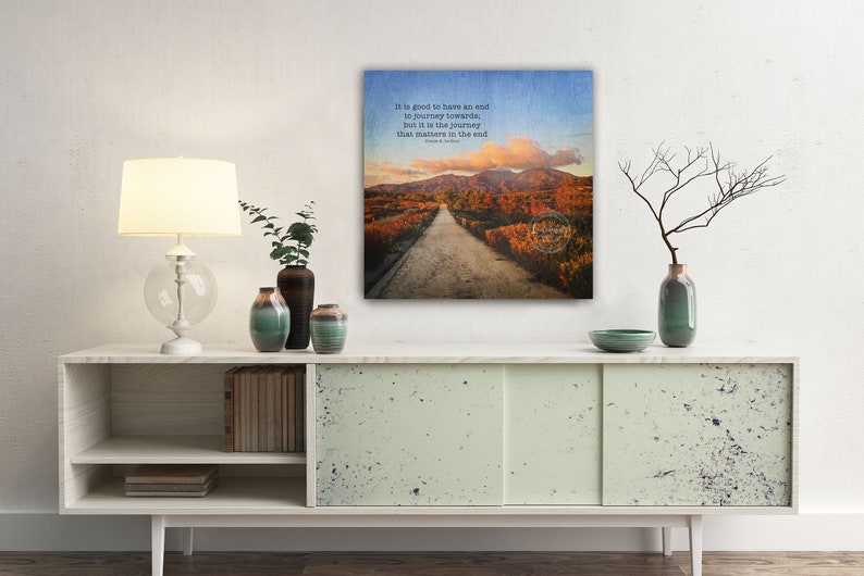 May include: A canvas print with a quote about the journey being more important than the destination. The quote is "It is good to have an end to journey towards, but it is the journey that matters in the end." The image shows a dirt road leading through a forest with fall foliage.