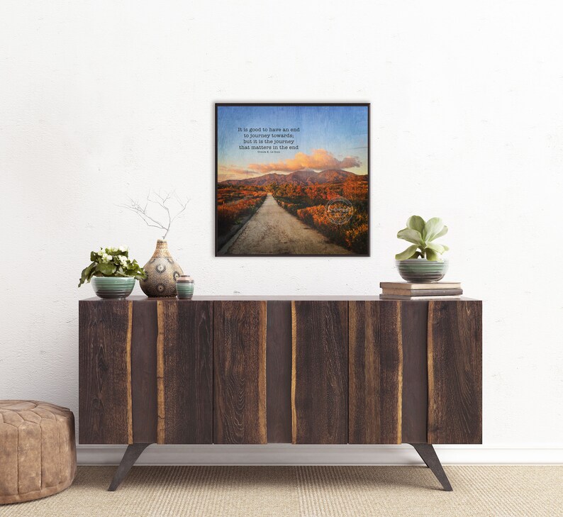 May include: A framed print with a quote about the importance of the journey, featuring a scenic road winding through a forest with colorful autumn foliage. The quote reads: "It is good to have an end to journey toward, but it is the journey that matters in the end."