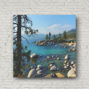 May include: A scenic view of a lake with large rocks and pine trees. The water is a vibrant turquoise blue and the sky is a clear blue with white clouds.