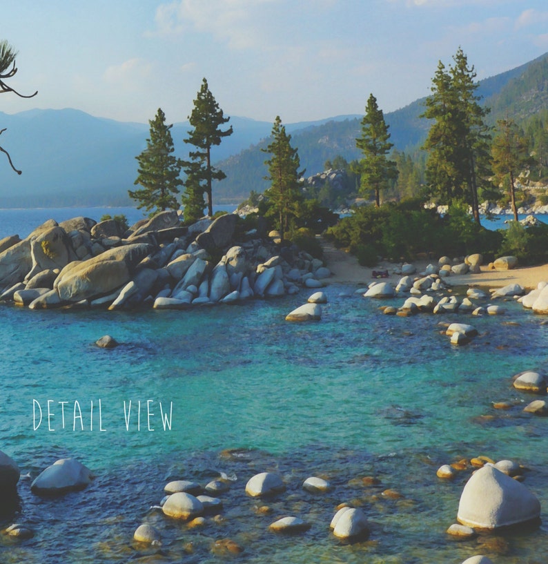 May include: A scenic view of a lake with large rocks and pine trees. The water is a vibrant turquoise blue and the sky is a clear blue. The text "DETAIL VIEW" is written in white on the bottom of the image.