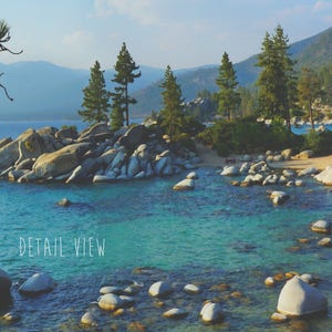May include: A scenic view of a lake with large rocks and pine trees. The water is a vibrant blue-green color. The text "DETAIL VIEW" is written in white on the bottom left of the image.