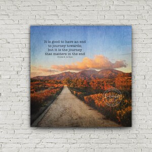 May include: A motivational quote by Ursula K. Le Guin about the importance of the journey, set against a scenic backdrop of a winding road leading through a landscape of hills and trees. The quote reads: "It is good to have an end to journey towards; but it is the journey that matters in the end."