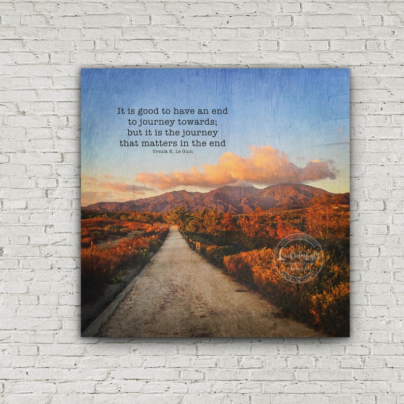 May include: A motivational quote by Ursula K. Le Guin about the importance of the journey, set against a scenic backdrop of a winding road leading through a landscape of hills and trees. The quote reads: "It is good to have an end to journey towards; but it is the journey that matters in the end."