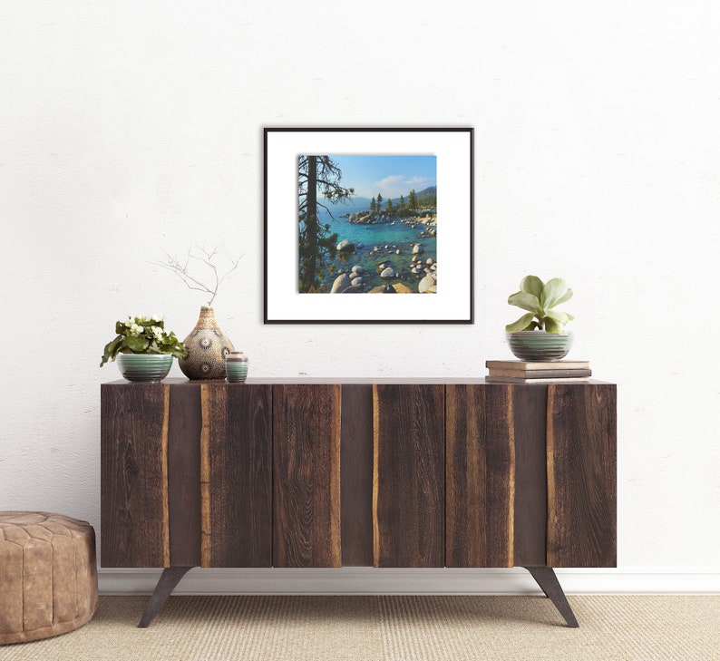 May include: A framed photograph of a scenic landscape with a lake, rocks, and trees. The lake is a vibrant blue-green color, and the rocks are scattered along the shoreline. The trees are green and lush, and the sky is a clear blue.