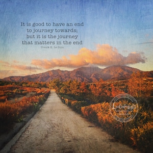 May include: A quote by Ursula K. Le Guin about the importance of the journey, set against a scenic backdrop of a winding path through a field of autumn foliage, leading towards a mountain range under a cloudy sky.
