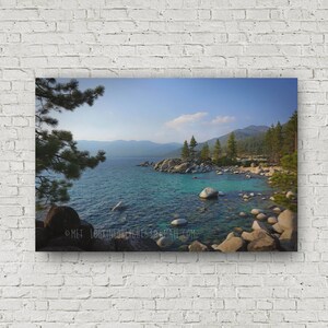May include: A panoramic view of Lake Tahoe, with a rocky shoreline and clear blue water. The mountains in the background are covered in trees and the sky is a bright blue.