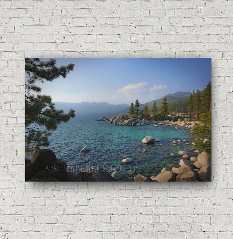 May include: A panoramic view of Lake Tahoe, with a rocky shoreline and clear blue water. The mountains in the background are covered in trees and the sky is a bright blue.