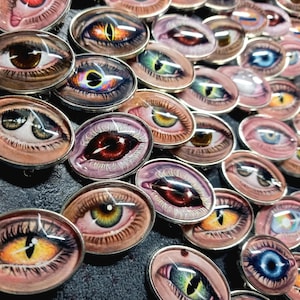 Peut inclure: Une collection d'épingles ovales sur le thème des yeux, avec des bordures en métal argenté. Les yeux présentent une variété de couleurs, dont le marron, le bleu, le vert et le jaune, avec des motifs détaillés d'iris et de pupilles. Les épingles sont disposées de près.