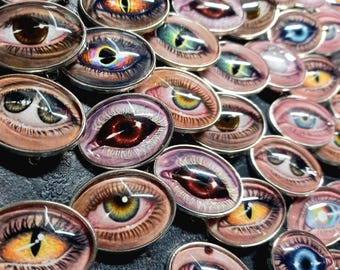 Peut inclure: Une collection d'épingles ovales sur le thème des yeux, avec des bordures en métal argenté. Les yeux présentent une variété de couleurs, dont le marron, le bleu, le vert et le jaune, avec des motifs détaillés d'iris et de pupilles. Les épingles sont disposées de près.
