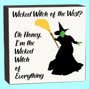 May include: A white wooden sign with black text and a silhouette of the Wicked Witch of the West. The text reads "Wicked Witch of the West? Oh Honey, I'm the Wicked Witch of Everything."