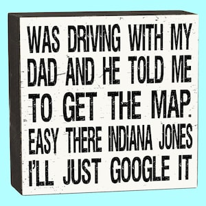 May include: White wooden box sign with black text that reads "Was driving with my dad and he told me to get the map. Easy there Indiana Jones I'll just google it."