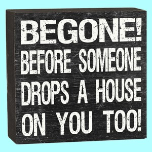 May include: Black wooden sign with white text that reads "BEGONE! BEFORE SOMEONE DROPS A HOUSE ON YOU TOO!"