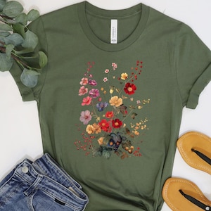 May include: A green short-sleeved t-shirt with a floral print featuring a variety of colors, including red, pink, yellow, blue, and green. The shirt is made of a soft, comfortable fabric and has a relaxed fit.