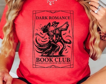 May include: Red t-shirt featuring a black graphic of skeletons dancing. The graphic reads "Dark Romance Book Club Always Falling for the Villain".