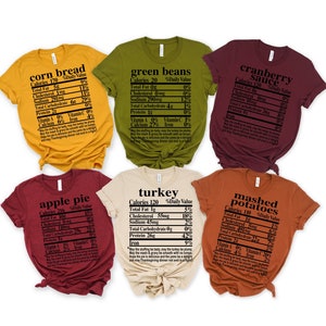 May include: Six short-sleeved t-shirts in various colors, each featuring a nutrition facts label for Thanksgiving foods like corn bread, green beans, and turkey. The text is in black, and the shirts are in shades of yellow, green, burgundy, beige, and orange.