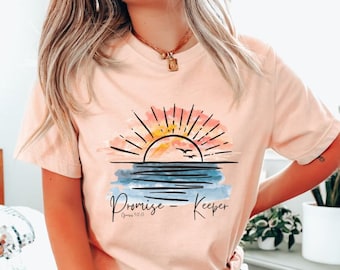 Puede incluir: Una camiseta rosa con un gráfico de puesta de sol acuarela y el texto "Promise Keeper" con la referencia bíblica "Génesis 1:26".