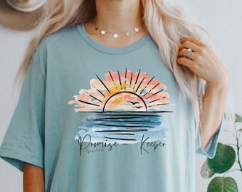 Puede incluir: Una camiseta azul claro con un gráfico de puesta de sol de acuarela y el texto "Promise Keeper" con la referencia bíblica "Romanos 12:13".