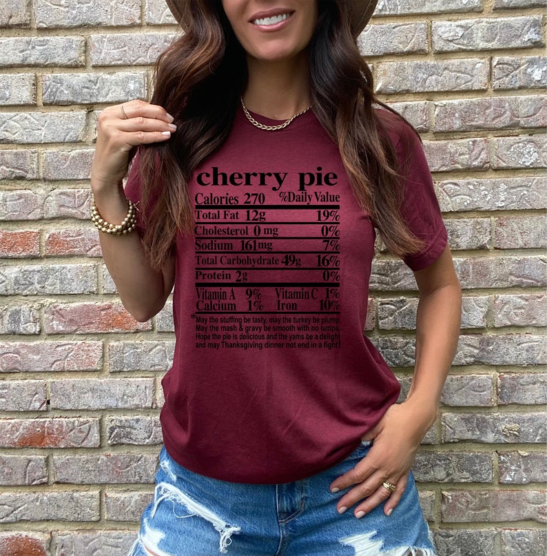 May include: Burgundy-colored t-shirt with the words "cherry pie" and a nutrition facts label printed on the front. The label lists calories, fat, cholesterol, sodium, carbohydrates, and protein content. A Thanksgiving-themed poem is printed below.