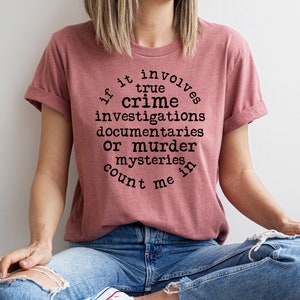 May include: A pink t-shirt with the text "If it involves true crime investigations documentaries or murder mysteries count me in" printed on it.